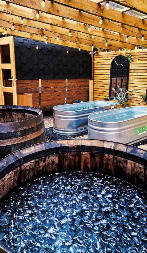 Ice-filled barrel and cold plunge tubs under festoon lights, with the sauna behind